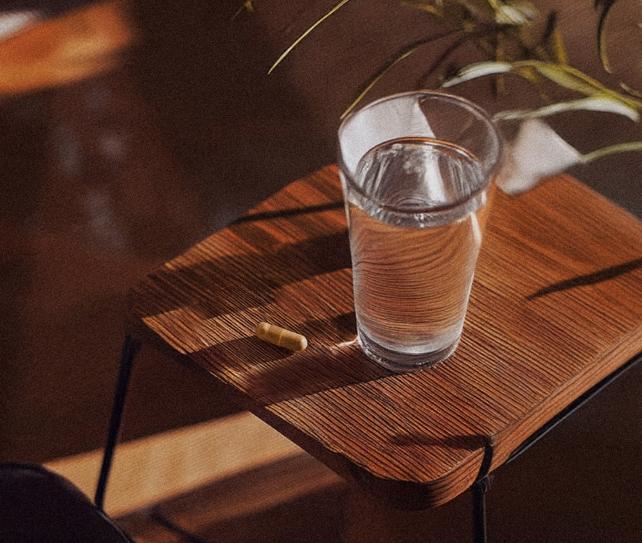 A capsule beside a glass of water on a sunlit wooden table